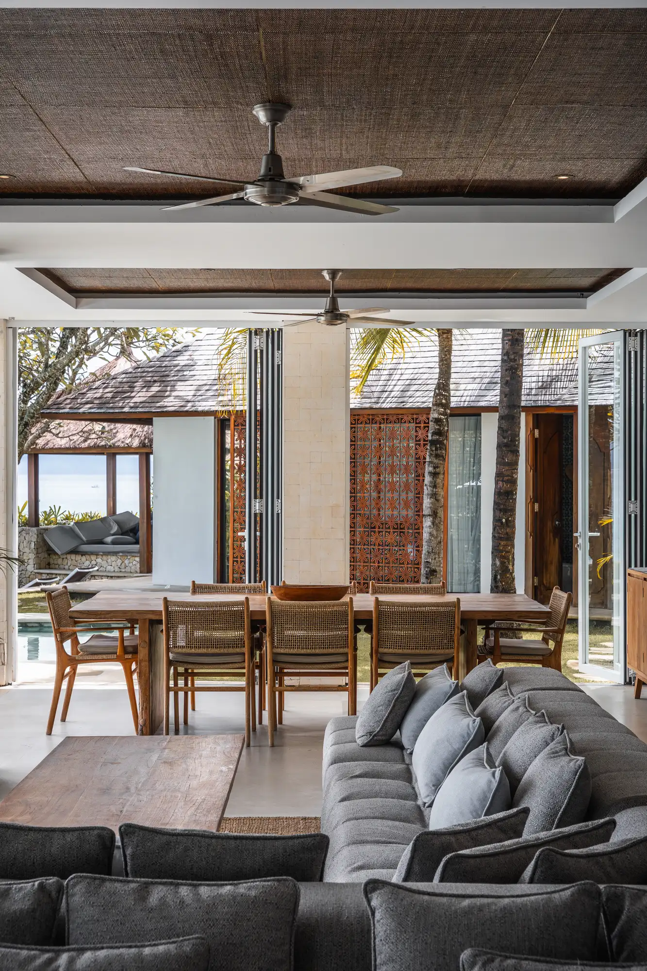 Dining table and sectional sofa opening to the pool through bifold doors at Lago Beach House Nusa Lembongan