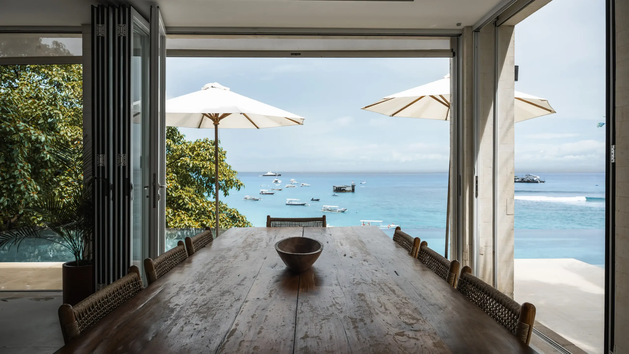 Dining table looking through open glass doors to Jungutbatu bay and Song Lambung beach at Lago Beach House
