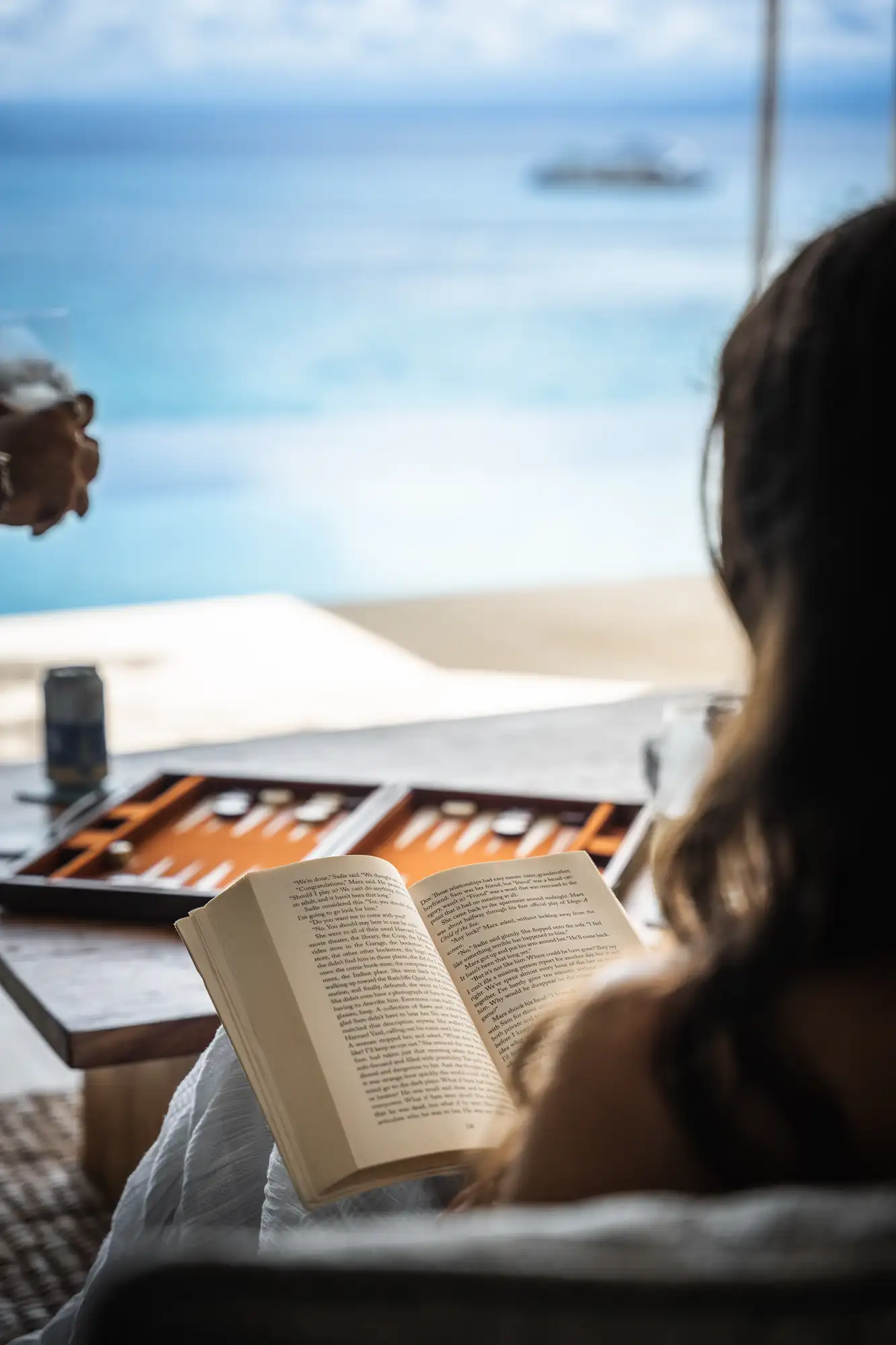 Guest reading a paperback with a backgammon board and ocean view at Lago Beach House Nusa Lembongan