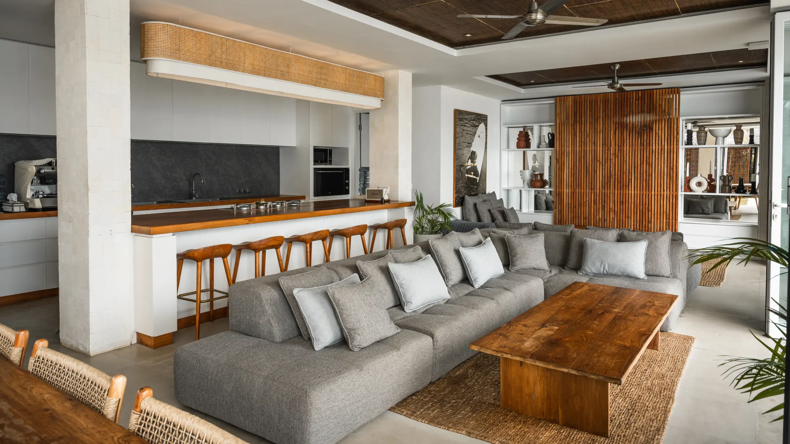 Open-plan kitchen with bar stools, sectional sofa and timber slat screen at Lago Beach House Nusa Lembongan