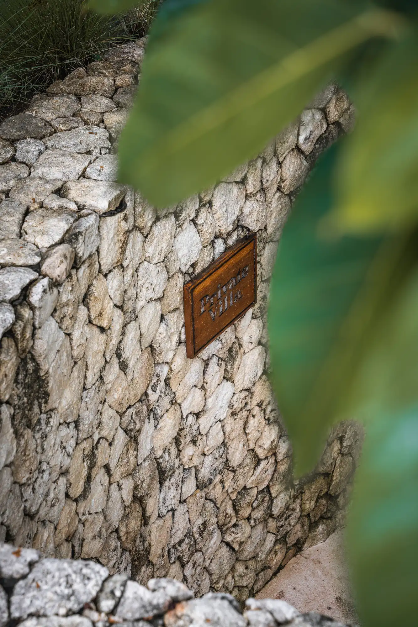Hand-laid limestone wall with villa plaque framed by tropical foliage at Lago Beach House