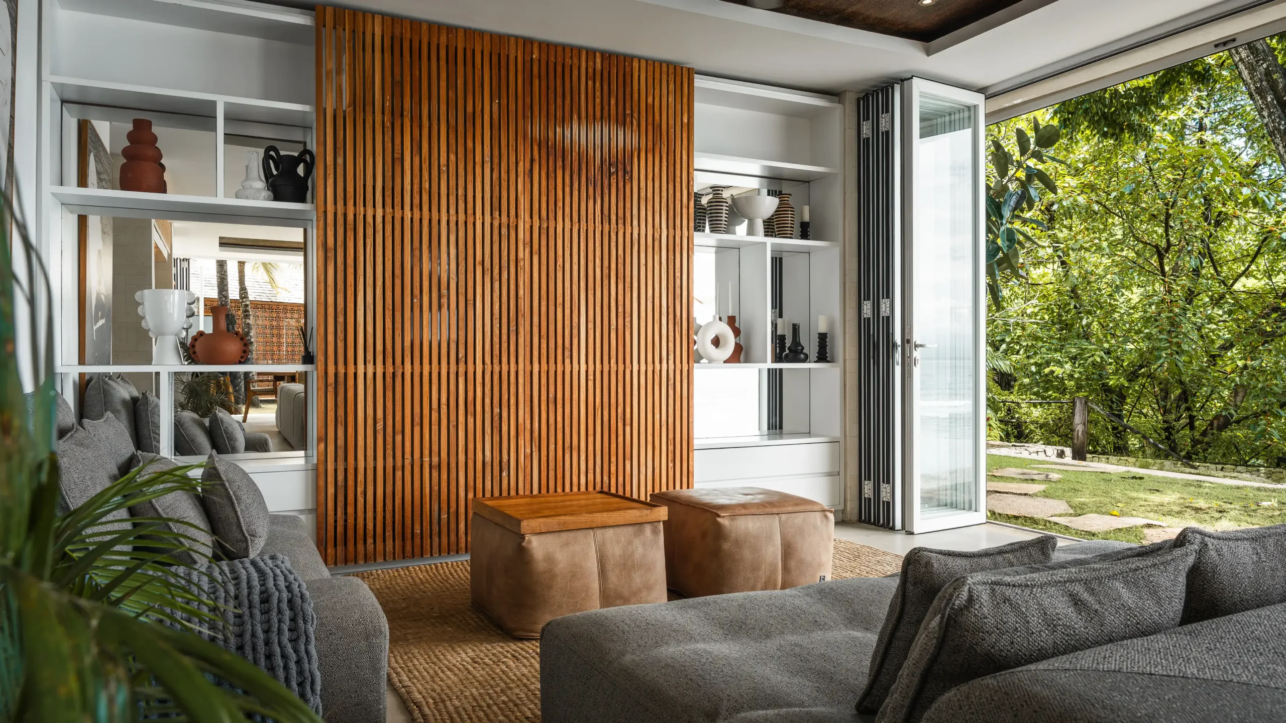 Living room with timber slat screen, leather ottomans and garden view at Lago Beach House Nusa Lembongan